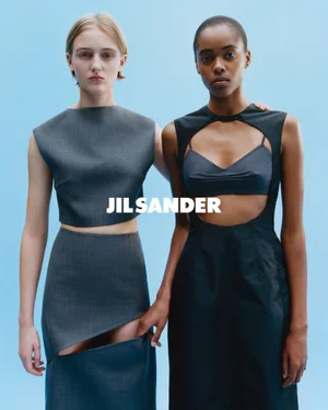 Two fashion models posing against a light blue backdrop for the Jil Sander SS 2026 campaign wearing dark grey architectural garments.