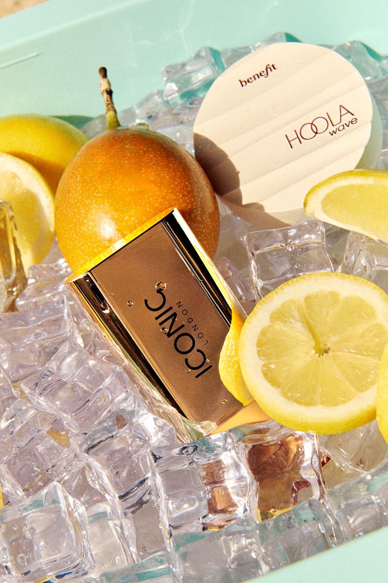 Close-up of bronze makeup palette, lemon slices, passionfruit, and Benefit Hoola Wave bronzer on a bed of clear ice cubes.
