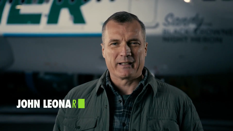 Man stands indoors wearing a jacket and plaid shirt, with an airplane in the background, and the name John Leonard on-screen.