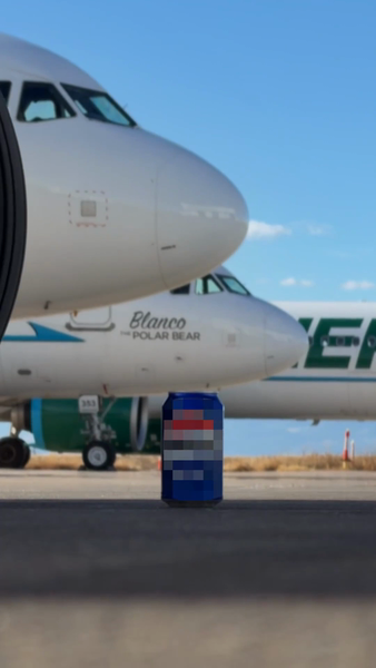 View of commercial airplanes on a tarmac, with a can of soda in the foreground on a sunny day, clear sky, and blurred background.