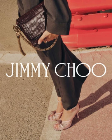 Fashion shot featuring a woman holding a dark brown crocodile-patterned clutch with gold chain, paired with pink high-heeled shoes outdoors.