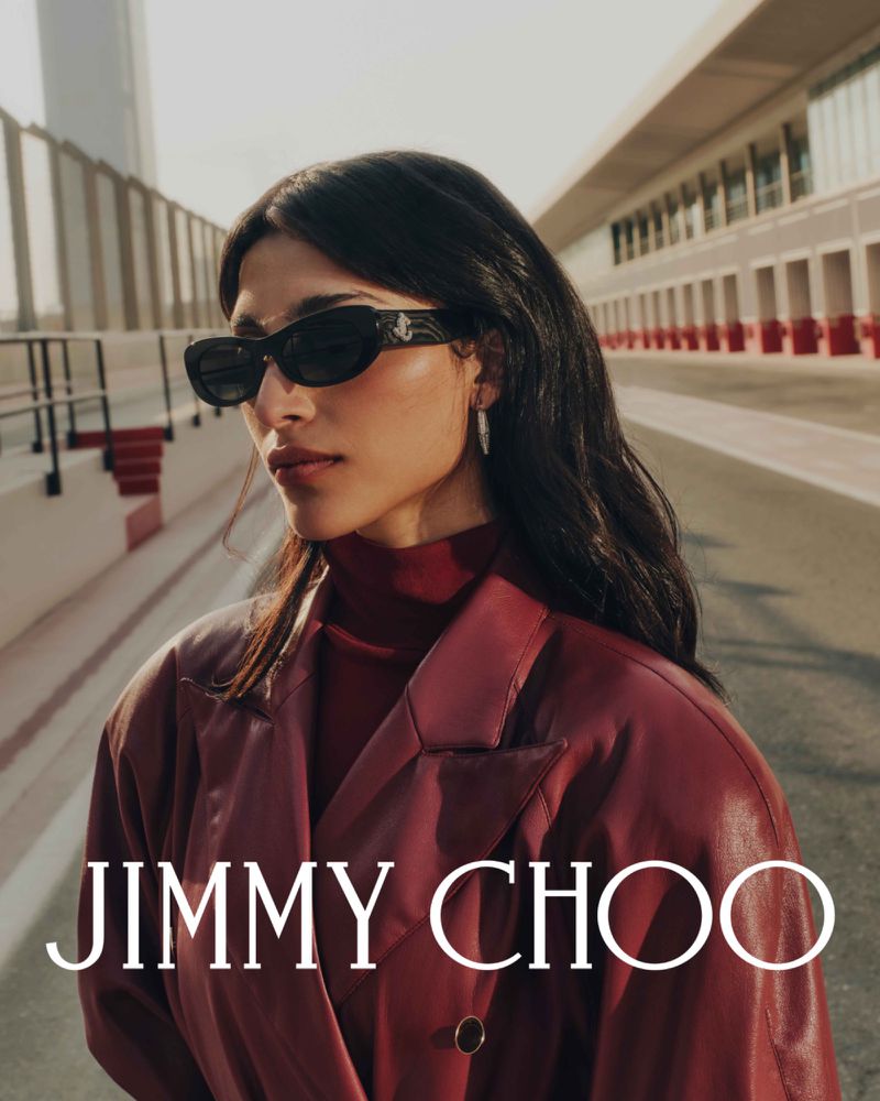 Fashion portrait of a woman in burgundy coat and sunglasses against an architectural backdrop, Jimmy Choo branding is visible.