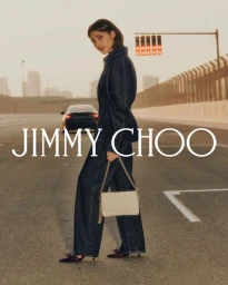 Woman in denim suit holding a cream shoulder bag on an empty asphalt road with a car and traffic light in the background
