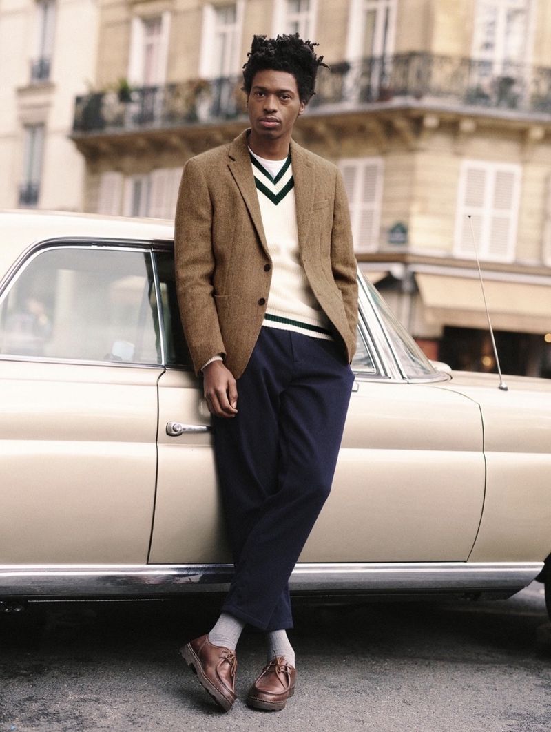 Stylish man in tweed blazer leans against vintage car on European street, showcasing classic fashion and urban lifestyle.