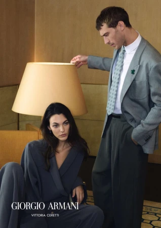 Model Vittoria Ceretti seated in front of a floor lamp next to a man in a grey suit for Giorgio Armani