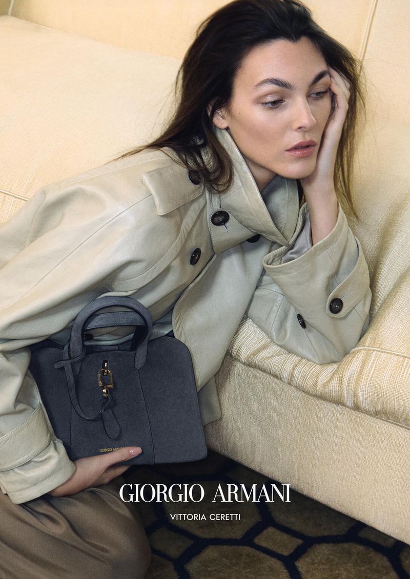 Model Vittoria Ceretti reclining on a sofa holding a grey handbag for Giorgio Armani S/S 2026 campaign.
