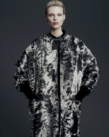 Woman in statement coat with gray and white abstract pattern, posing against a neutral gray backdrop in a fashion photography studio.