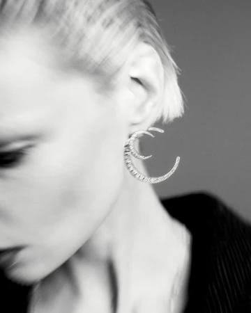 Close-up monochrome portrait of a model wearing distinctive crescent-shaped earrings against a grey background.