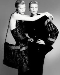 Two female models posing in black textured designer garments against a grey studio seamless backdrop