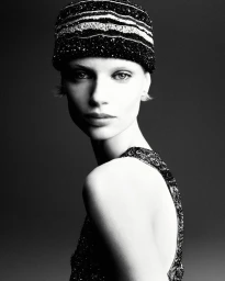 Monochrome portrait of a model wearing a beaded cap and dark patterned top against a dark background
