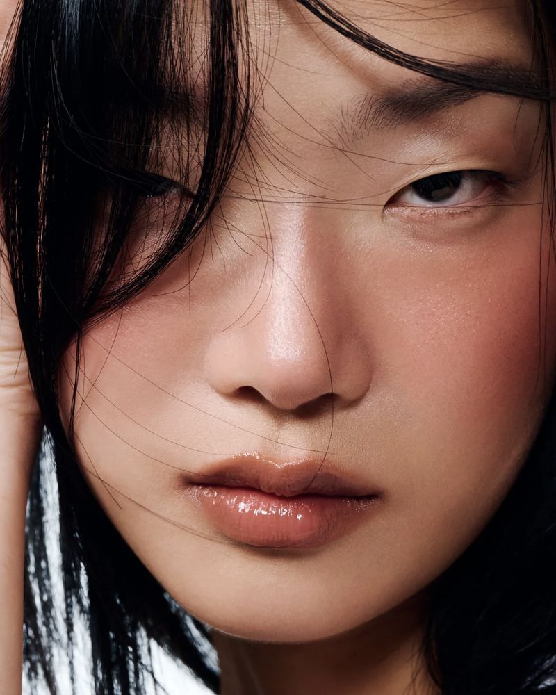 Close-up portrait of an Asian woman with glossy lips and black hair against a white background, emphasizing beauty and natural lighting.