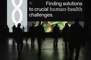 Silhouetted figures walking past a large screen displaying the text Finding solutions to crucial human health challenges