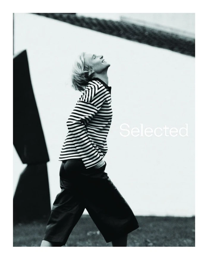 Model in a black and white striped long sleeve top walking outdoors with architectural background for Selected campaign.