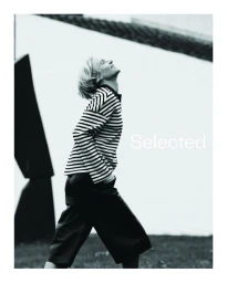 Model in a black and white striped long sleeve top walking outdoors with architectural background for Selected campaign.