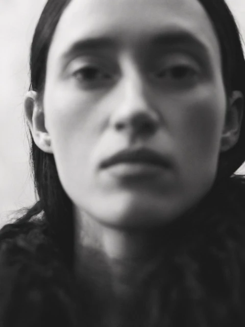 Black and white portrait of a young adult woman with straight dark hair, featuring a blurred background and shallow depth of field.