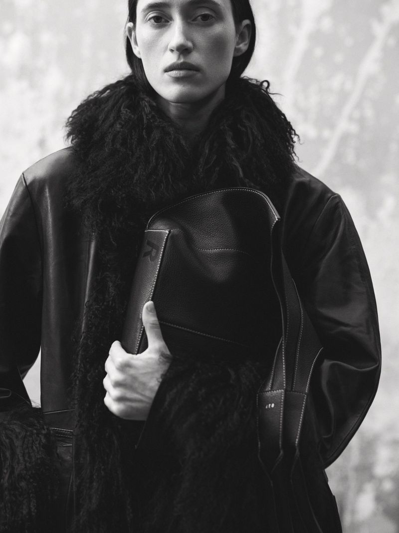 Model Helena Severin holding a dark leather bag while wearing a textured shearling collar coat in a black and white editorial portrait.