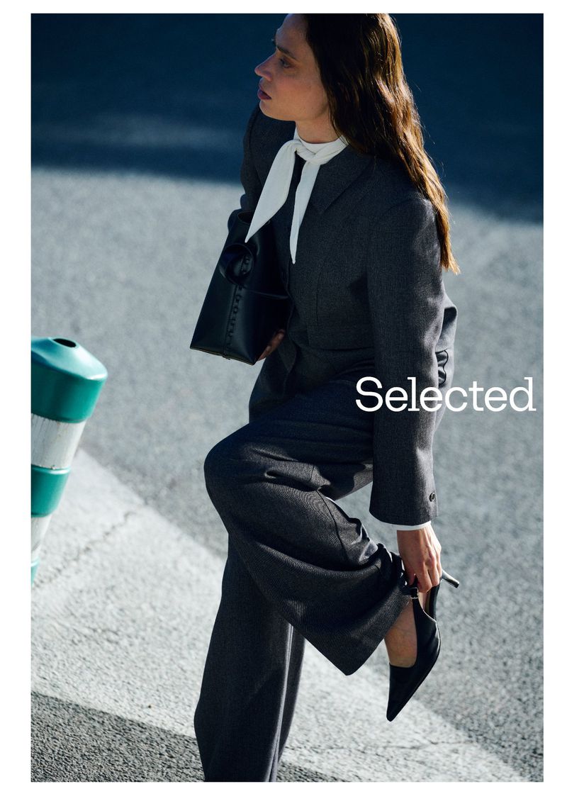 Model in charcoal grey suit adjusting her black heel against an asphalt background for Selected FW Campaign