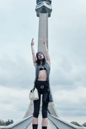 Model with arms raised stands on a bridge before a tall concrete tower for Samsøe Samsøe spring summer 2026 campaign.