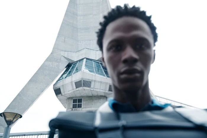 Low-angle portrait of a man outdoors with a tall concrete tower in the background for Samsøe Samsøe S/S 2026 campaign.