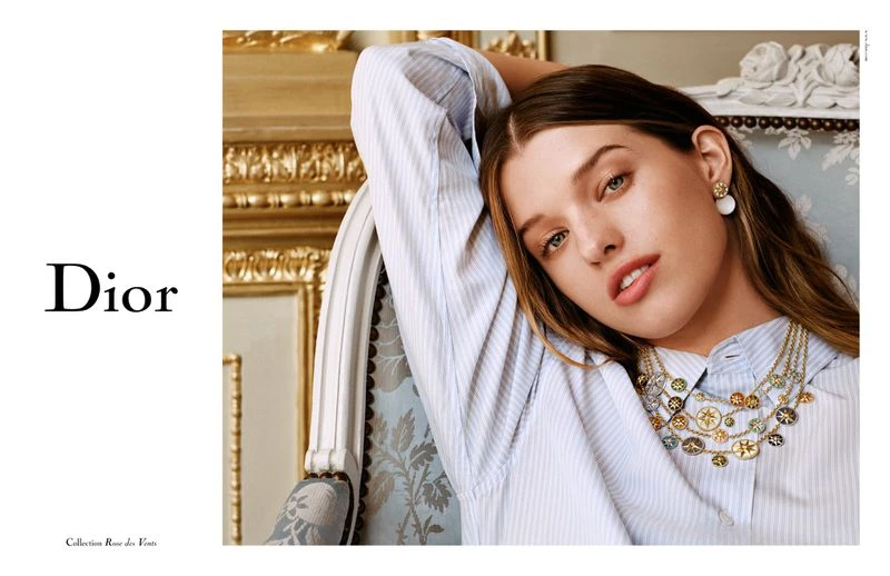 Close-up shot of a woman wearing a striped shirt and an ornate necklace, with the Dior logo and text visible on a white backdrop.