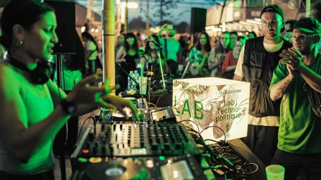 DJ mixing music on a turntable console at an outdoor nighttime festival event with crowds watching