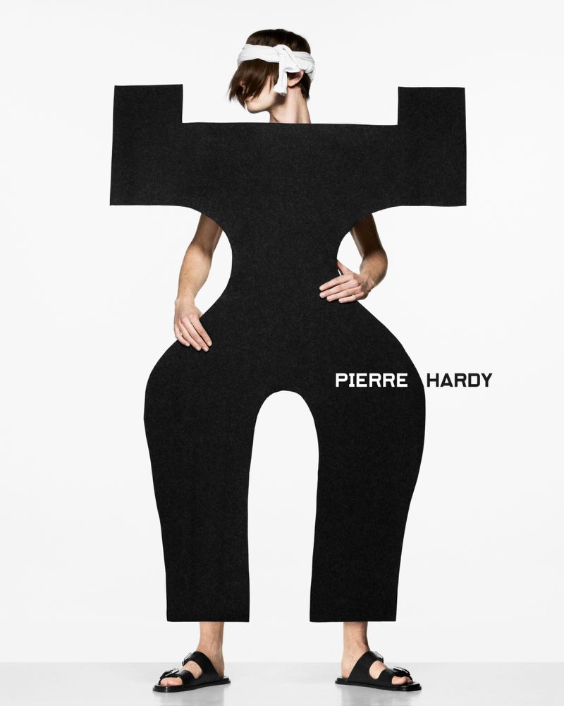 Fashion model in an abstract black costume and head wrap posing in a white photo studio for a Pierre Hardy advertisement.