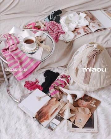 Still life on a bed with women's clothing, shoes, jewelry, magazines, a cup of tea, and a lamp creates a relaxed, fashion-themed scene.