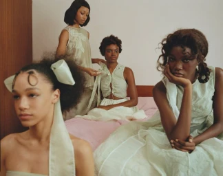 Four Black female models in pale green and white garments posing in a bedroom setting for Cecilie Bahnsen.