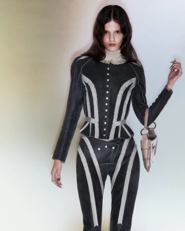 A slender woman in a striped jacket and pants poses in a studio with a handbag, showcasing a high-fashion editorial style.