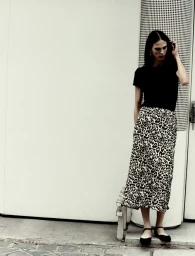 Model in black t-shirt and patterned skirt standing against a white wall for Massimo Dutti pre-fall