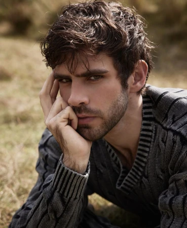Man resting his chin on his hand wearing a grey knit sweater in an outdoor setting for Harper's Bazaar Mexico.