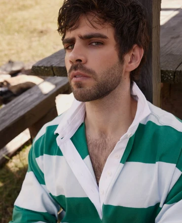 Close-up portrait of man with dark hair and stubble wearing a green and white striped rugby shirt outdoors.