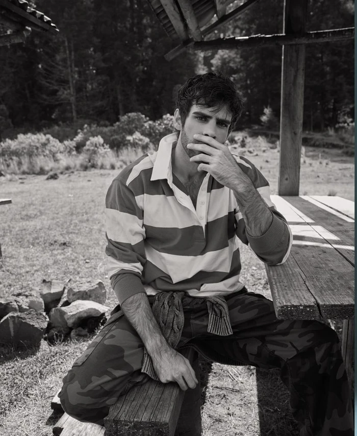 Monochrome portrait of a man sitting at a wooden picnic table wearing a striped rugby shirt and camo pants