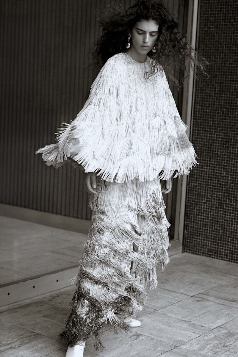 Woman posing in a shimmering fringe dress and earrings, captured in a monochrome shot against a textured wall and door.