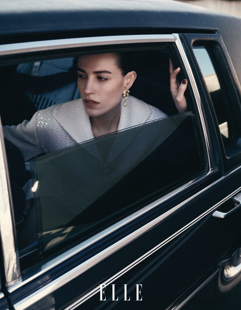 Portrait of a woman looking out the car window. She's wearing a light coat and elegant earrings, with the 'ELLE' logo visible.