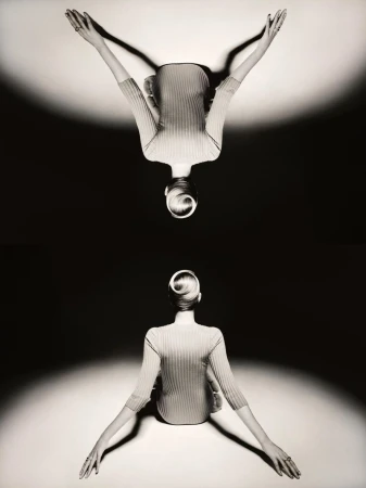 Mirrored studio shot of an adult woman with her arms raised above her head. She wears a ribbed top. The background is gradated.