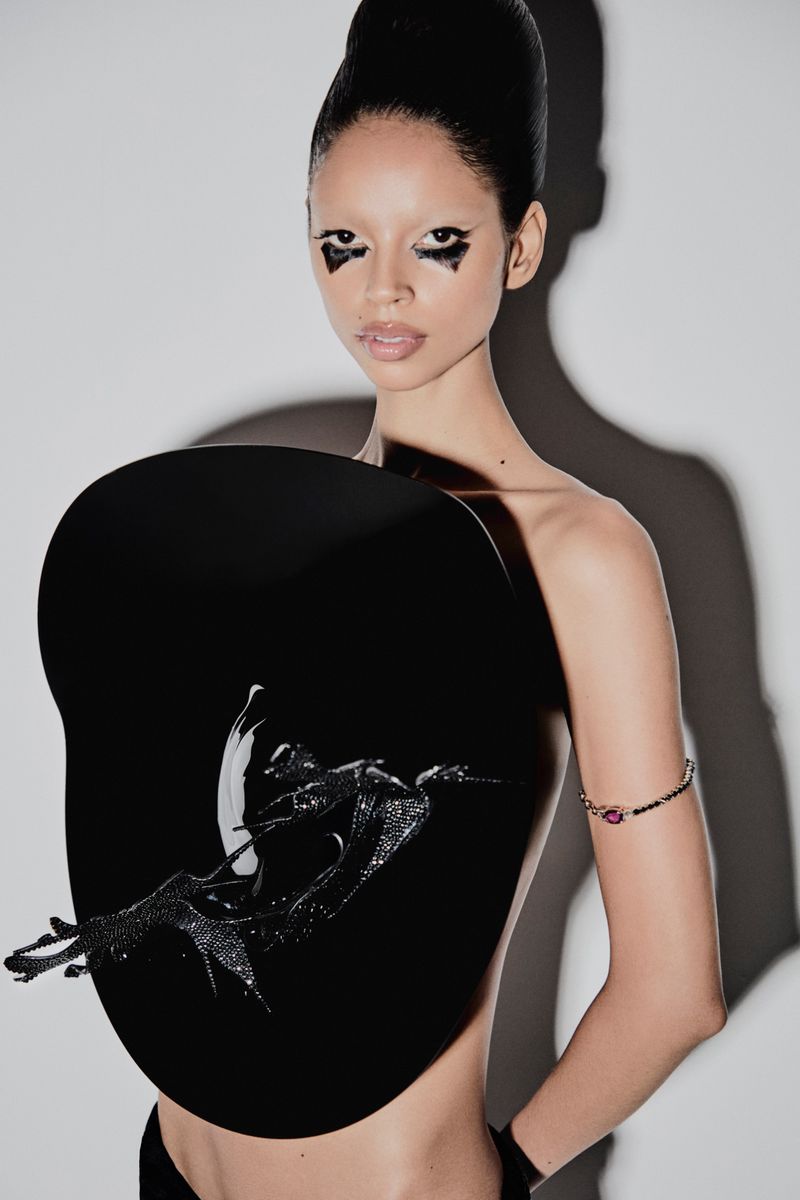Striking fashion portrait of a slender adult female with black graphic eye makeup, wearing a circular black avant-garde top in a studio.