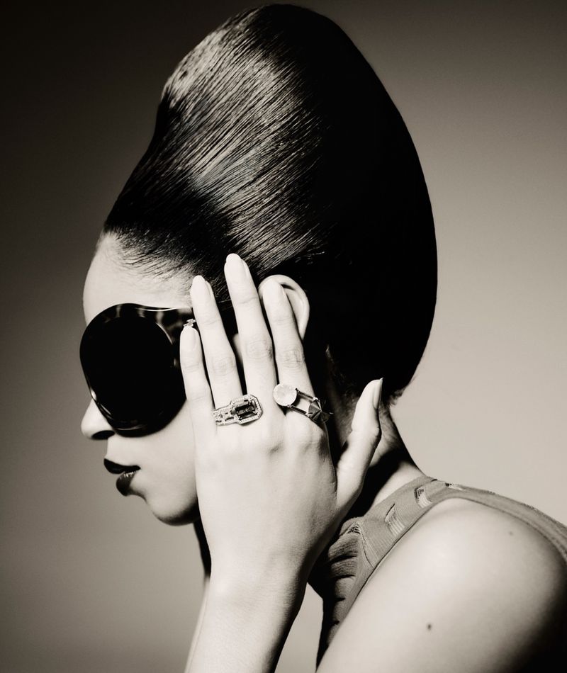 Portrait of an adult woman with an elegant hairstyle and sunglasses, wearing rings, in a studio with soft, neutral lighting.