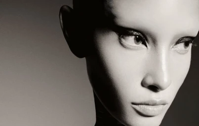 Close up monochrome portrait of a model with dramatic winged eyeliner against a plain dark grey studio background.