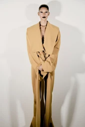 Model wearing a tan structured coat with long draped ties against a bright white background for Numero Switzerland