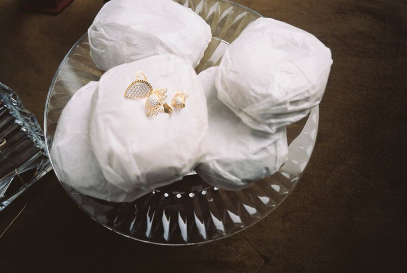 Close-up of gold jewelry, including a pendant and ring, arranged on crumpled white tissue paper inside of a clear glass bowl.