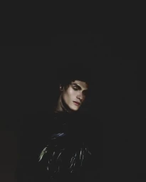 Close-up portrait of a male model with dark hair against a dark moody background for Numero Netherlands