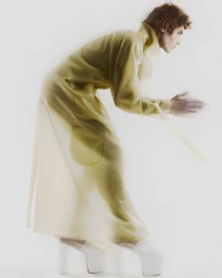 Profile shot of a male model in a translucent yellow coat and white platform shoes against a white background