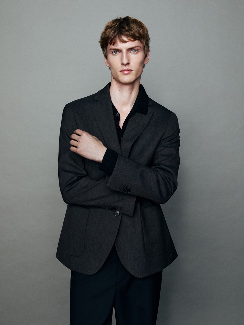 A man in a dark grey blazer standing against a plain grey backdrop for Massimo Dutti Quiet Tailoring.