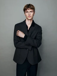 A man in a dark grey blazer standing against a plain grey backdrop for Massimo Dutti Quiet Tailoring.