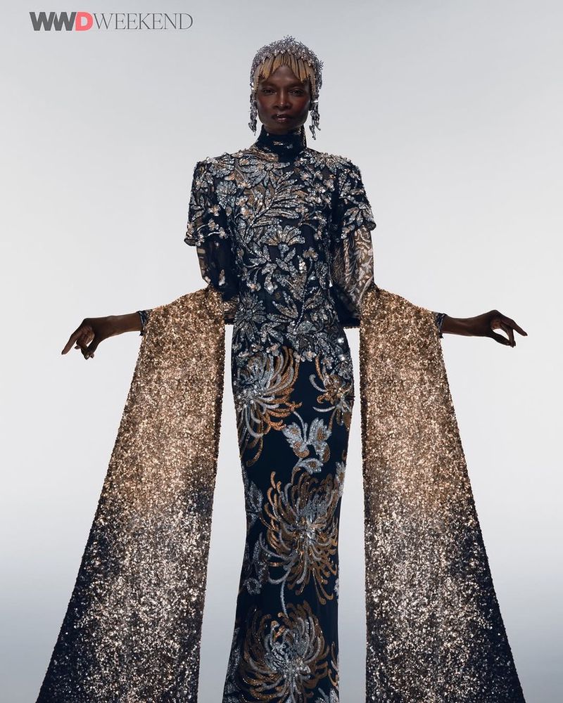 Elegant African woman poses in high-fashion sequin gown with statement sleeves and decorative headpiece against a neutral studio backdrop.