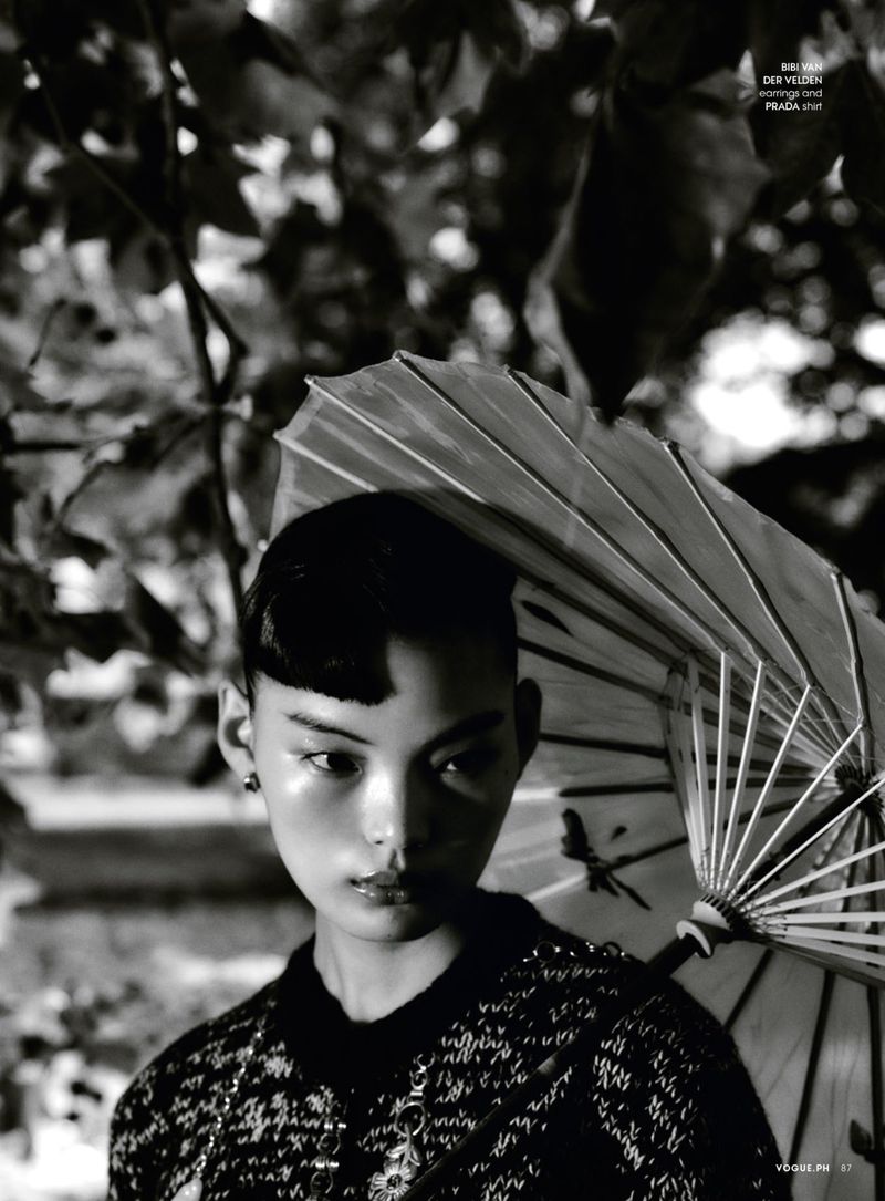 Portrait of an Asian woman with an umbrella in a black and white fashion editorial shot with a lush leafy background.