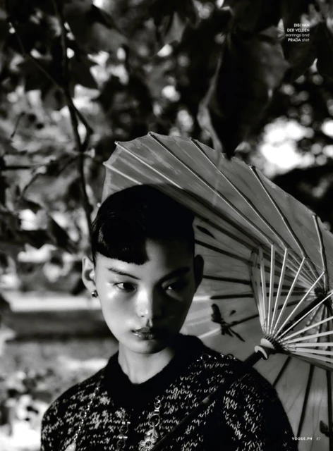 Portrait of an Asian woman with an umbrella in a black and white fashion editorial shot with a lush leafy background.