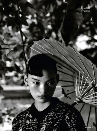 Portrait of an Asian woman with an umbrella in a black and white fashion editorial shot with a lush leafy background.