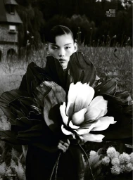 Model holding a massive sculptural dark flower arrangement in an outdoor garden setting